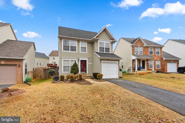 traditional-style home featuring a residential view, aphalt driveway, an attached garage, fence, and a front lawn