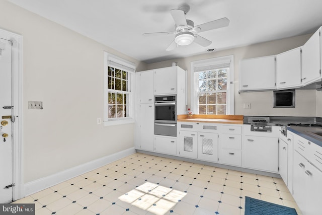 kitchen featuring light floors, white cabinets, a warming drawer, and oven