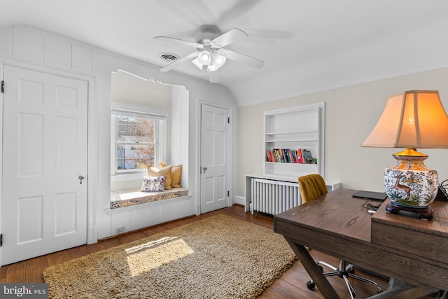 office space with built in shelves, wood finished floors, visible vents, a ceiling fan, and radiator heating unit