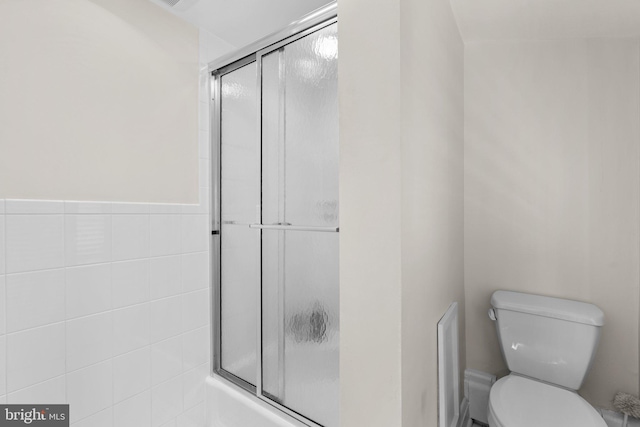 bathroom with toilet, combined bath / shower with glass door, and tile walls