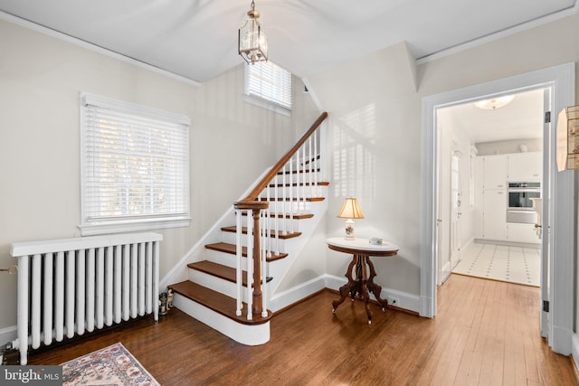 stairs with radiator heating unit, crown molding, baseboards, and hardwood / wood-style floors