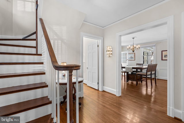 staircase featuring ornamental molding, wood-type flooring, a notable chandelier, and baseboards