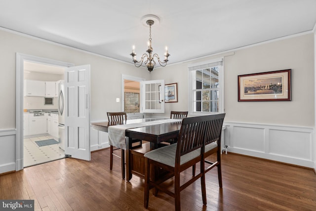 dining area with hardwood / wood-style flooring, a wainscoted wall, ornamental molding, a decorative wall, and a notable chandelier