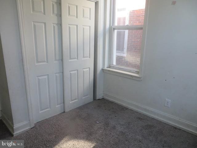 unfurnished bedroom featuring multiple windows, a closet, and dark colored carpet