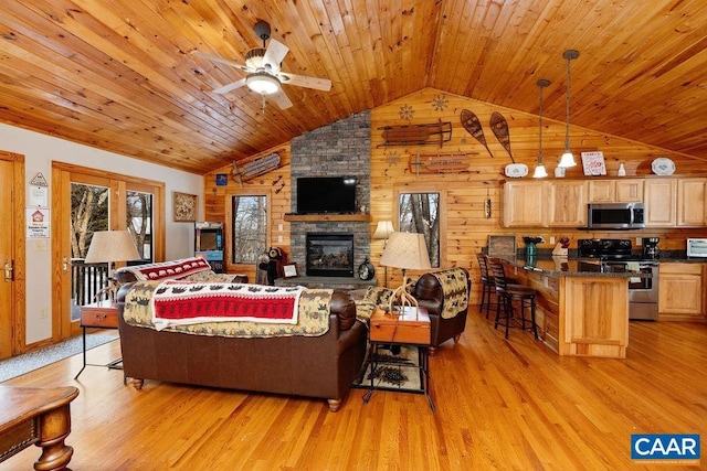 living room featuring light hardwood / wood-style flooring, ceiling fan, a stone fireplace, vaulted ceiling, and wood walls