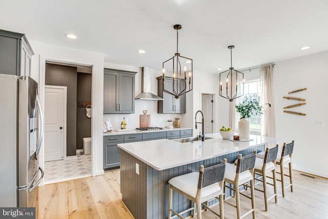 kitchen featuring appliances with stainless steel finishes, decorative light fixtures, an island with sink, sink, and wall chimney range hood