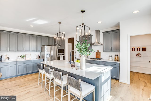 kitchen with an island with sink, a kitchen bar, hanging light fixtures, stainless steel appliances, and wall chimney range hood