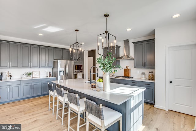 kitchen featuring appliances with stainless steel finishes, a breakfast bar, decorative light fixtures, wall chimney range hood, and a center island with sink
