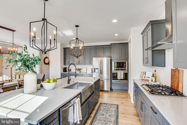 kitchen featuring decorative light fixtures, light wood-type flooring, gray cabinets, stainless steel appliances, and wall chimney range hood