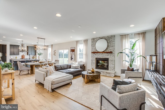 living room featuring an inviting chandelier, a fireplace, light hardwood / wood-style flooring, and a healthy amount of sunlight
