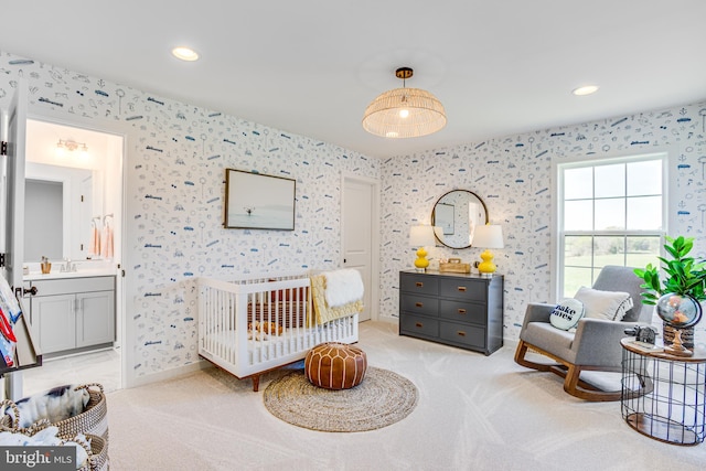 bedroom featuring ensuite bath, sink, light carpet, and a crib