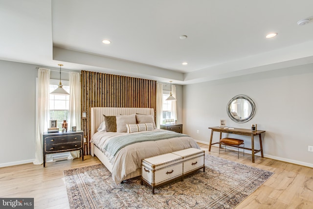 bedroom with multiple windows, a tray ceiling, and light hardwood / wood-style flooring