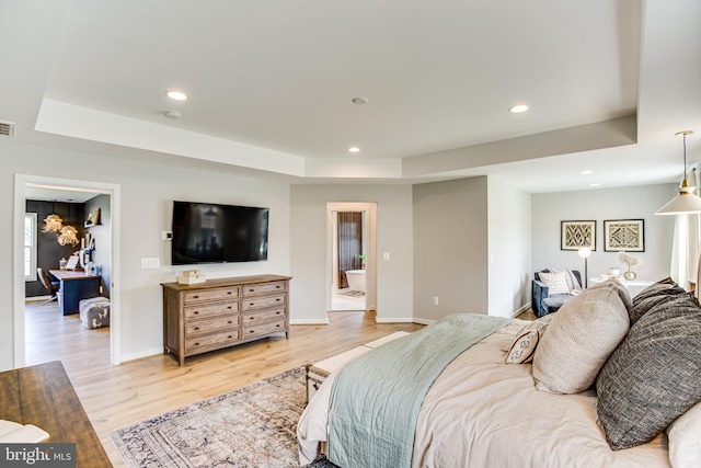 bedroom featuring connected bathroom, light wood-type flooring, and a tray ceiling
