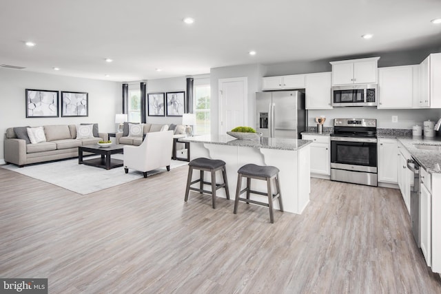 kitchen with a breakfast bar area, white cabinetry, light stone counters, a kitchen island, and stainless steel appliances