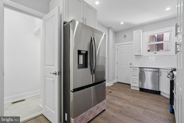 kitchen featuring white cabinetry, hanging light fixtures, appliances with stainless steel finishes, hardwood / wood-style floors, and decorative backsplash