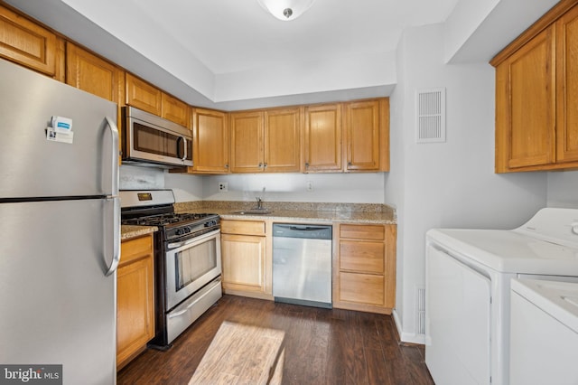 kitchen with appliances with stainless steel finishes, dark hardwood / wood-style flooring, separate washer and dryer, and sink