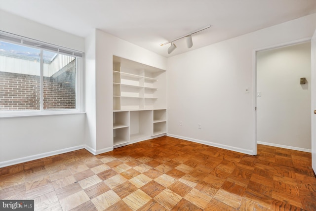 empty room featuring rail lighting, parquet flooring, and built in shelves