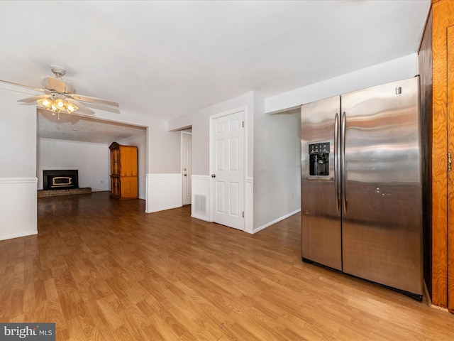 kitchen featuring stainless steel fridge with ice dispenser, a fireplace, ceiling fan, and light wood-type flooring