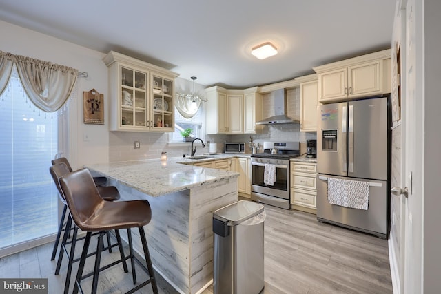 kitchen with sink, stainless steel appliances, decorative light fixtures, kitchen peninsula, and wall chimney exhaust hood