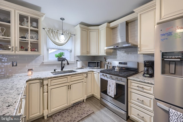 kitchen with appliances with stainless steel finishes, pendant lighting, sink, cream cabinets, and wall chimney exhaust hood