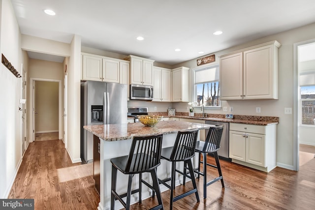 kitchen featuring stainless steel appliances, a center island, light wood finished floors, and light stone countertops