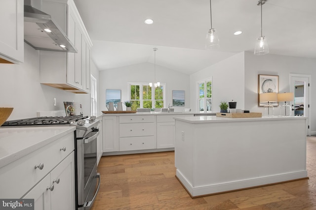 kitchen with lofted ceiling, light countertops, wall chimney range hood, white cabinetry, and gas stove