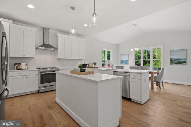 kitchen with a peninsula, a kitchen island, light countertops, appliances with stainless steel finishes, and wall chimney exhaust hood