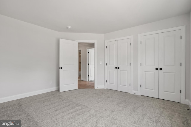 unfurnished bedroom with baseboards, two closets, and carpet flooring