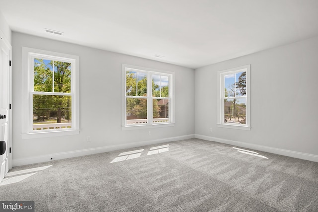 empty room featuring a wealth of natural light, visible vents, and carpet