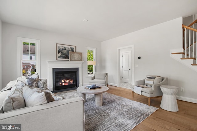 living room with a fireplace with flush hearth, wood finished floors, baseboards, and stairs