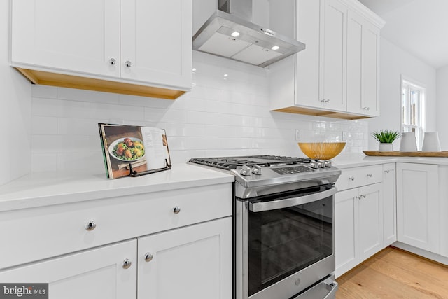 kitchen featuring light wood finished floors, light countertops, white cabinetry, gas range, and wall chimney exhaust hood