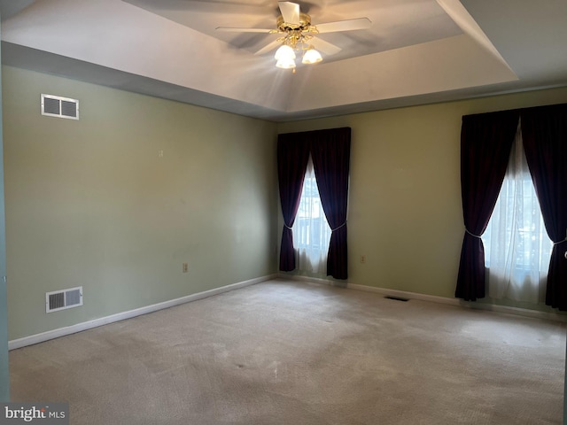 empty room with light colored carpet, a raised ceiling, and ceiling fan