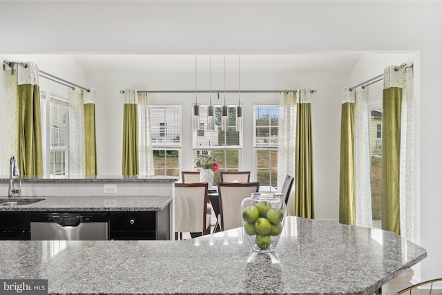 kitchen featuring light stone counters, hanging light fixtures, stainless steel dishwasher, and sink