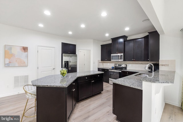 kitchen with stainless steel appliances, kitchen peninsula, a breakfast bar area, and light wood-type flooring