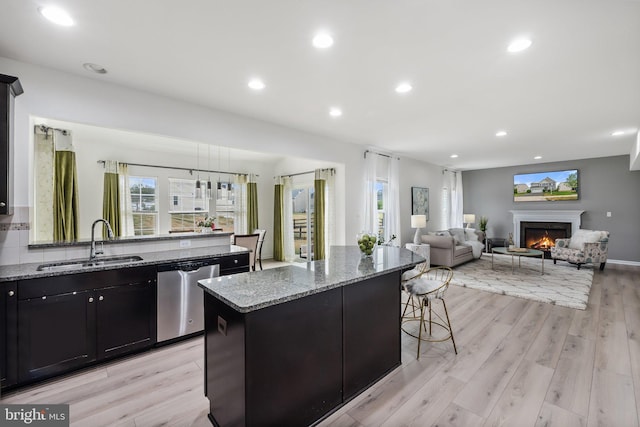 kitchen featuring sink, a center island, light wood-type flooring, dishwasher, and light stone countertops