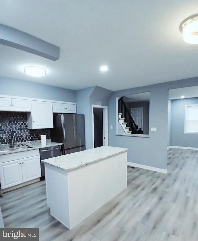 kitchen with stainless steel appliances, a sink, white cabinets, light wood-type flooring, and backsplash