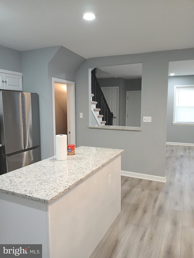 kitchen featuring light stone counters, white cabinets, stainless steel refrigerator, and light hardwood / wood-style floors