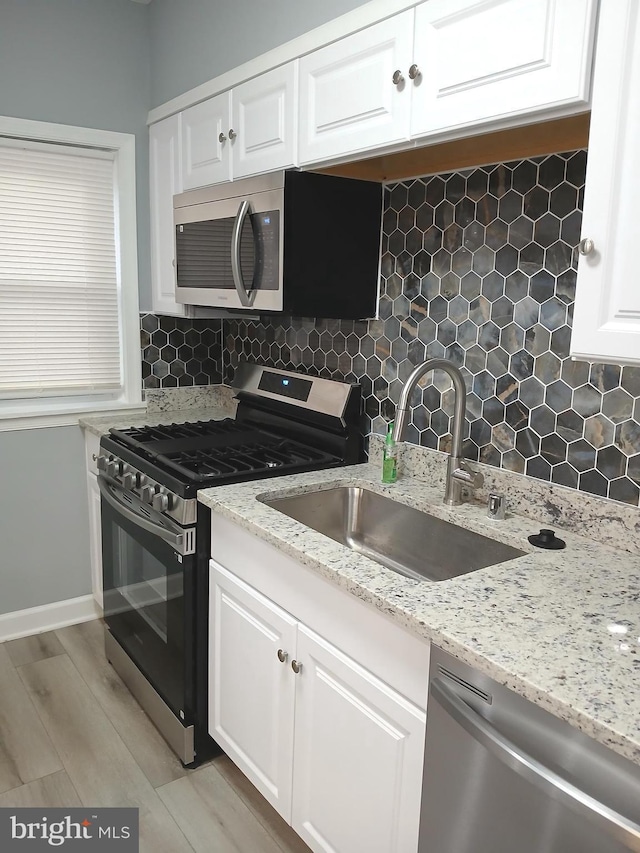 kitchen featuring stainless steel appliances, a sink, white cabinetry, and decorative backsplash