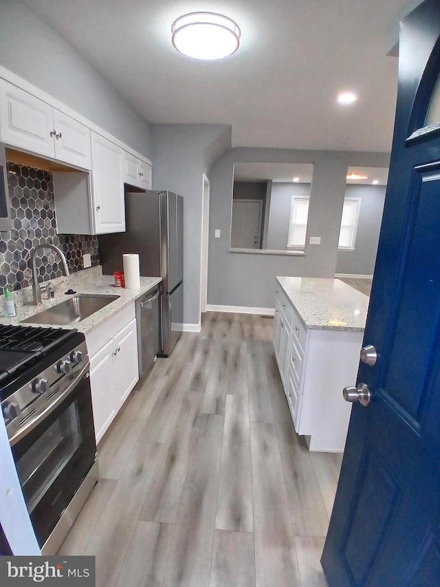 kitchen featuring stainless steel appliances, light wood-style flooring, decorative backsplash, white cabinets, and a sink