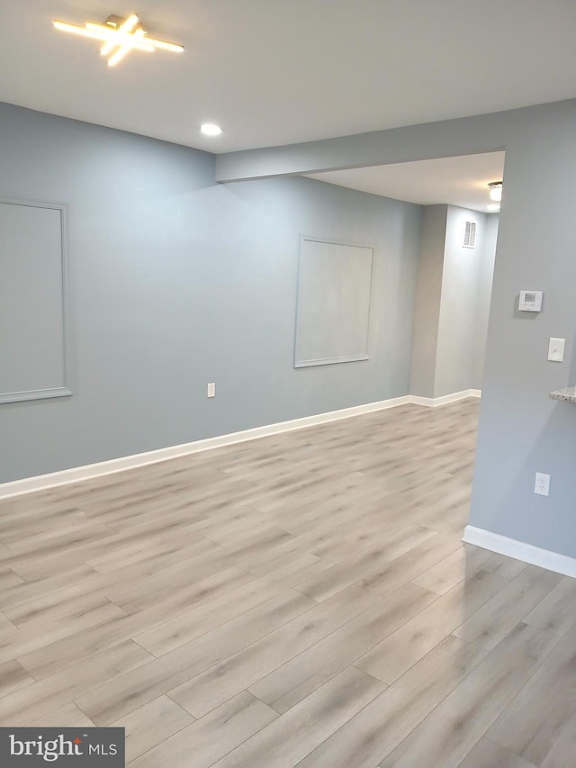 finished basement with light wood-style floors, visible vents, and baseboards