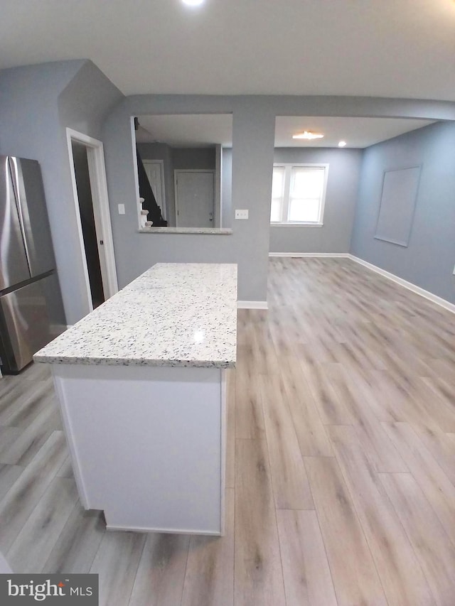 kitchen with light stone counters, baseboards, freestanding refrigerator, a center island, and light wood finished floors