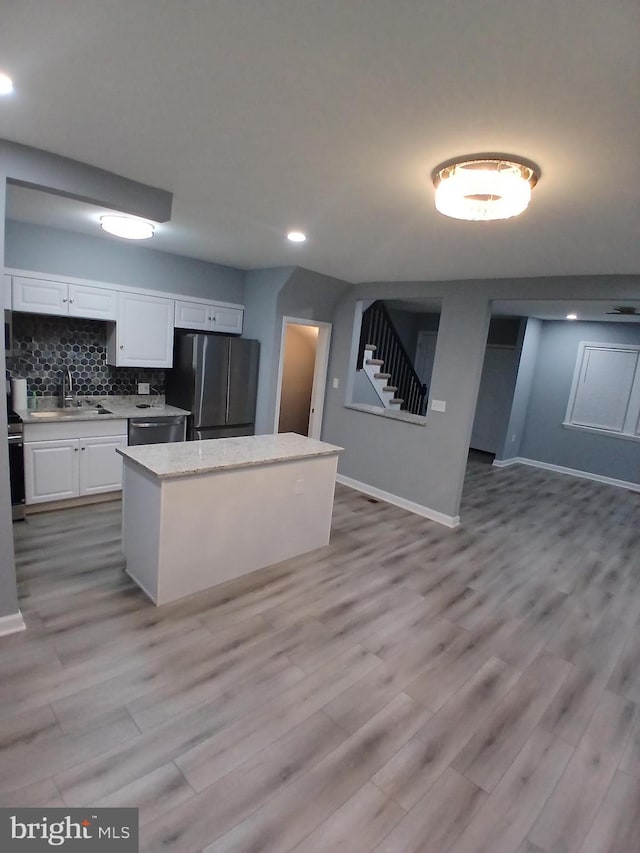 kitchen featuring white cabinets, appliances with stainless steel finishes, a center island, a sink, and backsplash