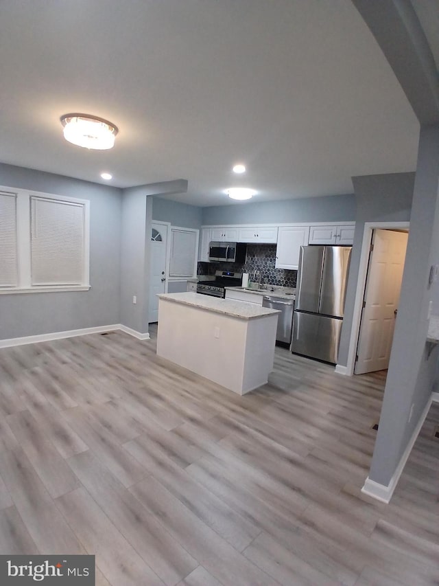 kitchen featuring a kitchen island, white cabinets, appliances with stainless steel finishes, backsplash, and light wood finished floors