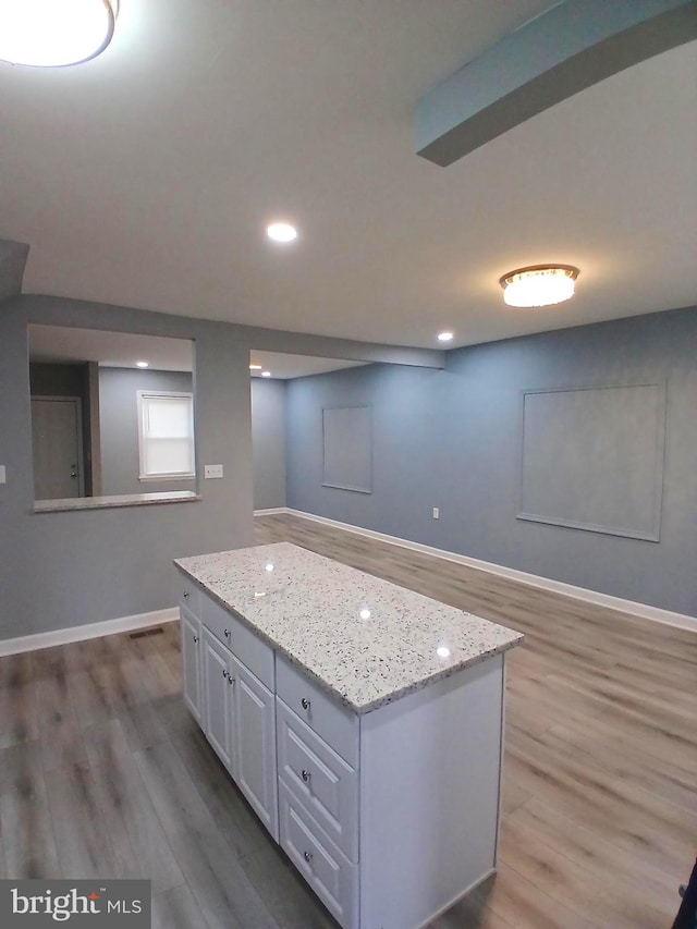 kitchen with wood-type flooring, a kitchen island, white cabinets, and light stone counters