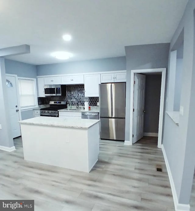 kitchen featuring stainless steel appliances, backsplash, light wood-style floors, white cabinets, and baseboards