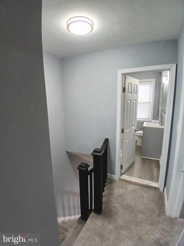 corridor featuring a sink, carpet flooring, and an upstairs landing