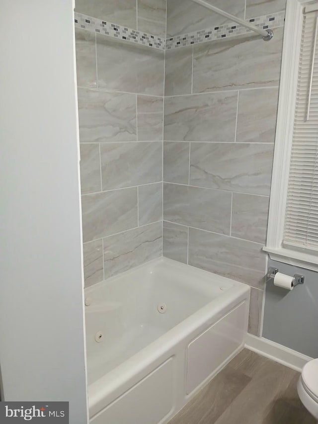 full bath with toilet, baseboards, wood finished floors, and a combined bath / shower with jetted tub