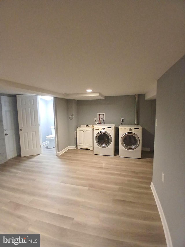 clothes washing area featuring independent washer and dryer, light hardwood / wood-style floors, and cabinets