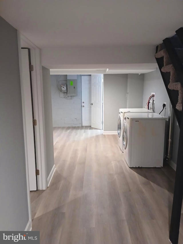 washroom featuring electric panel, washer and clothes dryer, and light hardwood / wood-style flooring