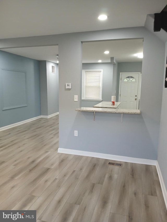 kitchen featuring recessed lighting, a breakfast bar, wood finished floors, baseboards, and light stone countertops